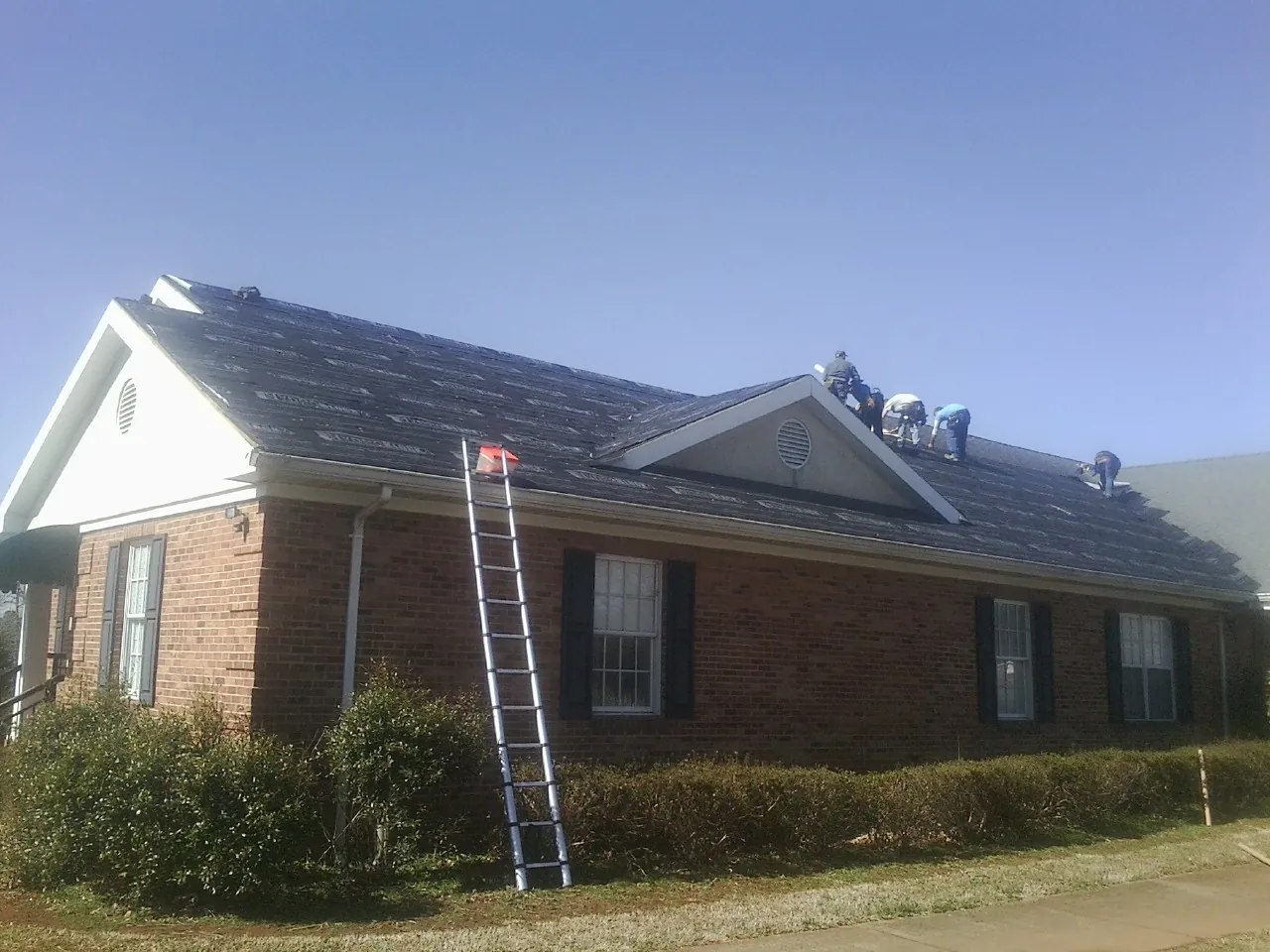 Crew tearing shingles off a brick ranch roof with a ladder set — Emergency Roof Repair work by our crew in Dorena