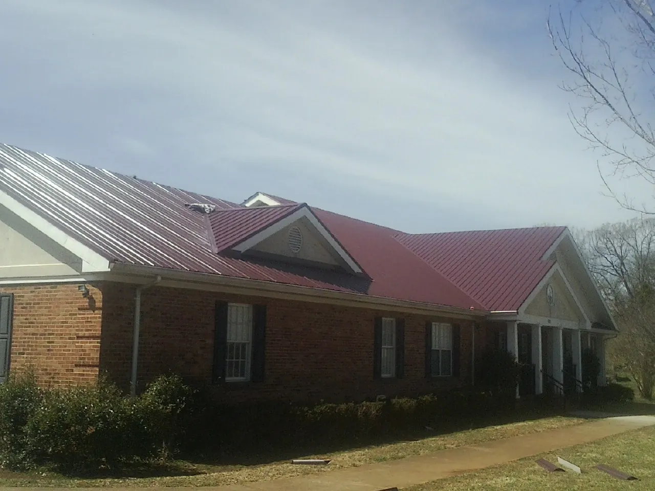 Red metal roof with gabled entries on a long brick building, from a Hail Damage Roof Repair job in Dorena