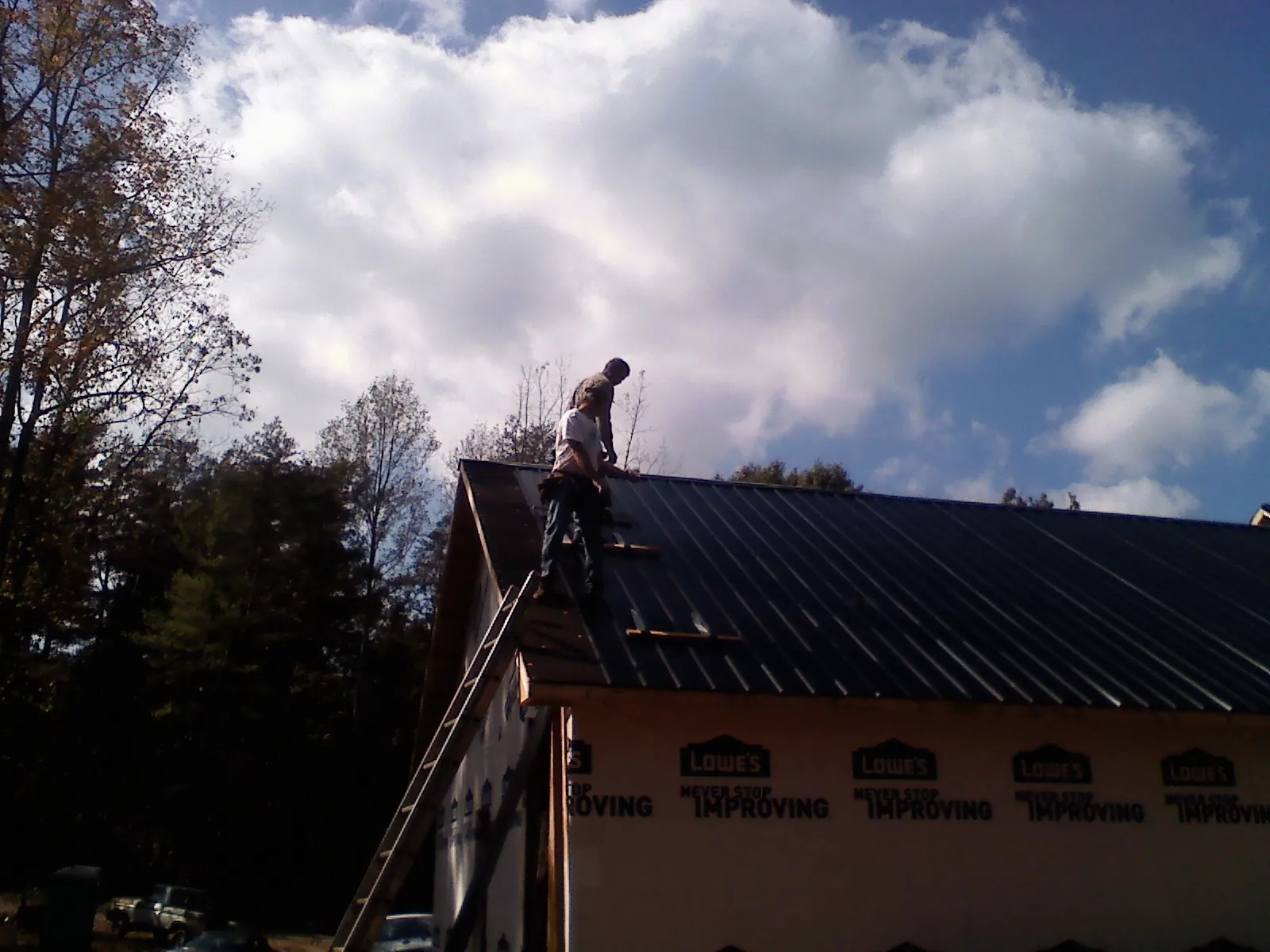 Roofer fastening dark metal panels high against a cloudy sky, from a Roof Inspection job in Dorena